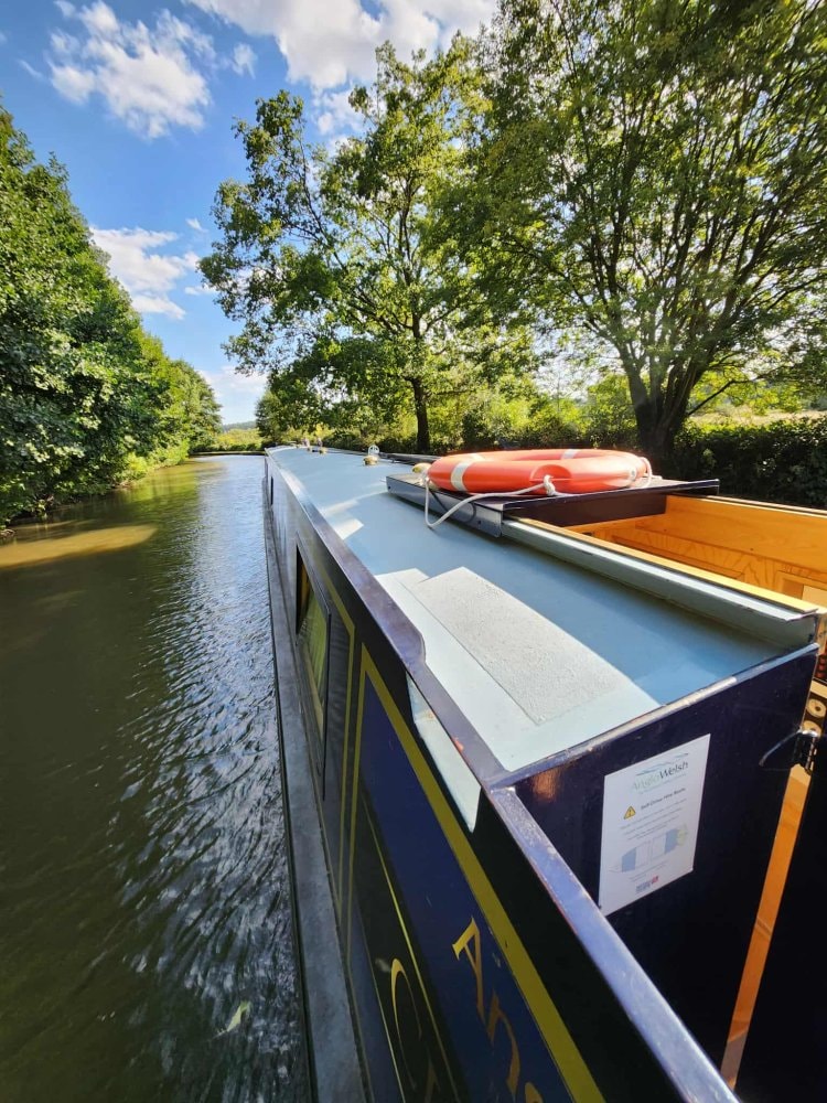 Narrowboat cruising a tree-lined English canal